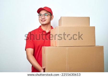 Dreamy smiling asian male courier in blue uniform, looking upper left corner excited and happy, carry boxes with orders, deliver parcels standing over white background Royalty-Free Stock Photo #2255630613
