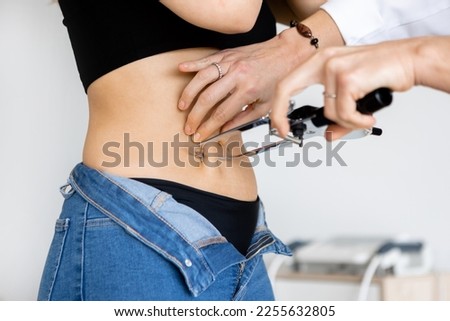 Crop nutritionist with caliper checking up thickness of skin fold on belly of slim woman in office. Close up, Horizontal