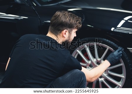 Man blackening of tire wheel of car using sponge with chemical blackening of rubber in detailing auto service. Back view. High quality photo