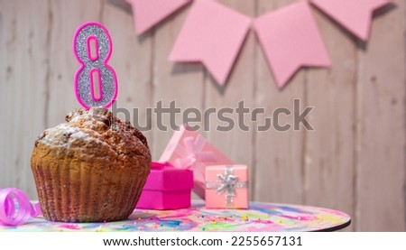 Festive cake or muffin with a pink candle with a number  8. Happy birthday background with a number for a girl or woman with beautiful decorations. Anniversary party copy space.