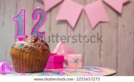 Festive cake or muffin with a pink candle with a number  12. Happy birthday background with a number for a girl or woman with beautiful decorations. Anniversary party copy space.