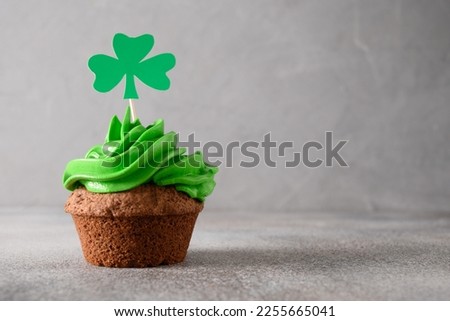 St. Patrick's Day cupcake with green whipped cream decorated clover on gray background. Copy space. Close up. Festive food.
