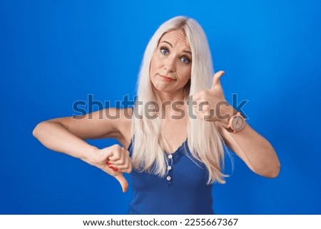 Caucasian woman standing over blue background doing thumbs up and down, disagreement and agreement expression. crazy conflict 