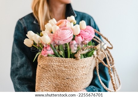 Woman holds a bouquet of white tulips and pastel pink and peach ranunculus in a jute bag.