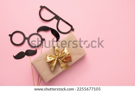 Flat lay view of packed Father`  s day present with mustache and glasses on pink background, lot of copy space. Fun greeting card mock up.