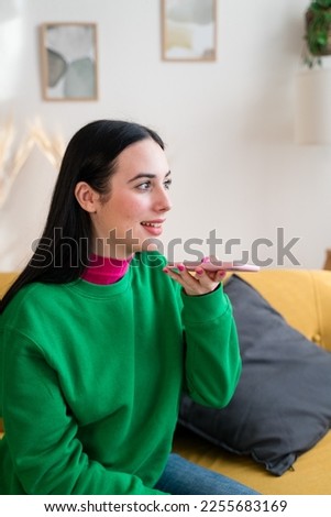 Young woman using smartphone in living room sending a voice note