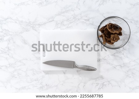 Flat lay. Cutting dehydrated wild mushrooms on a white cutting board. Royalty-Free Stock Photo #2255687785