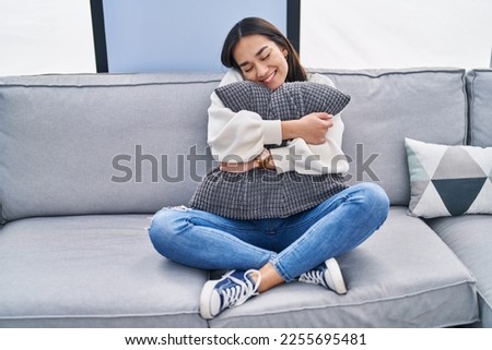 Young hispanic woman hugging cushion sitting on sofa at home