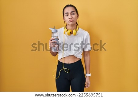 Young south asian woman wearing sportswear drinking water looking sleepy and tired, exhausted for fatigue and hangover, lazy eyes in the morning. 