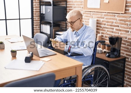 Young caucasian man business worker using smartphone sitting on wheelchair at office