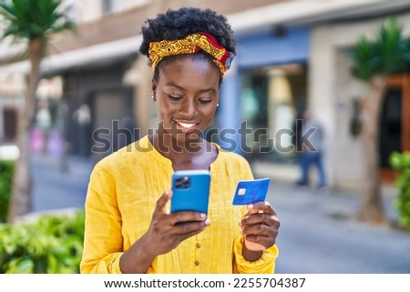 Young african american woman using smartphone and credit card at street