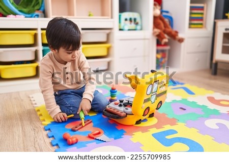 Adorable hispanic boy playing with technician tools toy sitting on floor at kindergarten Royalty-Free Stock Photo #2255709985