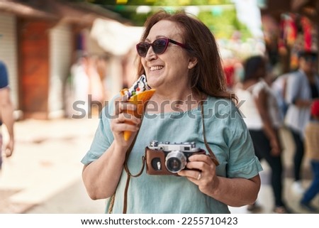 Senior woman tourist holding camera eating ice cream at street