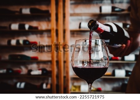 Waiter pouring red wine in glasses for wine on the table in restaurant