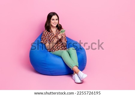 Full length photo of youngster attractive girl wear vintage shirt chatting online smartphone sit beanbag relax isolated on pink color background
