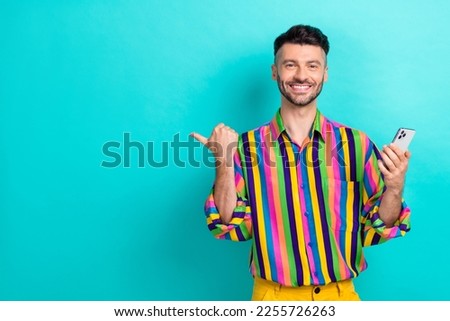 Photo of good mood positive man brunet hair dressed striped shirt indicating empty space hold phone isolated on turquoise color background