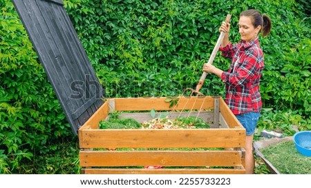 Making compost from organic waste in the garden. A woman stirs waste in a wooden compost bin with a pitchfork. Using kitchen waste to make compost. Increasing the fertility and aeration of the soil. Royalty-Free Stock Photo #2255733223