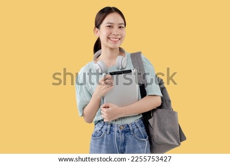 Happy Young Asian student girl holding tablet computer over isolated yellow background.