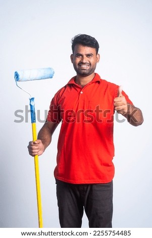 Vertical shot of smiling painter with paint roller brush showing thumbs up sign by looking camera - concept of professional service, employment and home renovation.