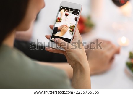 Cropped over shoulder shot of young brunette woman taking photo on cell phone while holding her fiance hand, female showing beautiful ring, romantic got engaged on valentines day, closeup