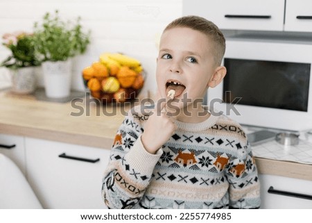 The boy licks the finger with the dough. Child helps mom to cook in the kitchen. Light modern home interior.