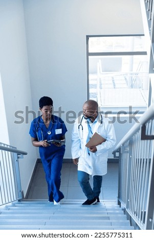 African american female and male doctor using tablet on hospital staircase with copy space. Hospital, medical and healthcare services.
