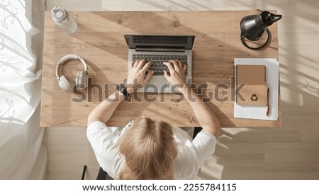 Top down view of girl working at computer, achieving success and joy. young woman throws her hands up in win or successful deal. blonde in white t-shirt rejoices while sitting at workplace.