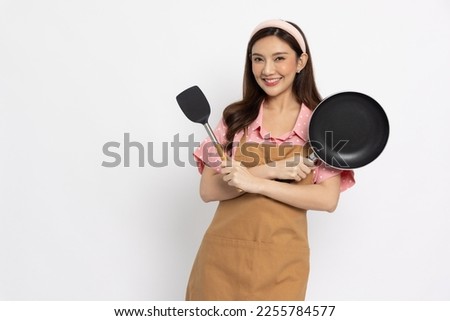 Young Asian woman housewife wearing kitchen apron cooking and holding pan and flipper isolated on white background Royalty-Free Stock Photo #2255784577