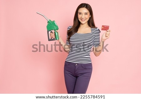 Happy young Asian woman holding payment card or credit card and used to pay for gasoline, diesel, and oil dispenser isolated on pink background, Driver with fleet cards for refueling car concept Royalty-Free Stock Photo #2255784591