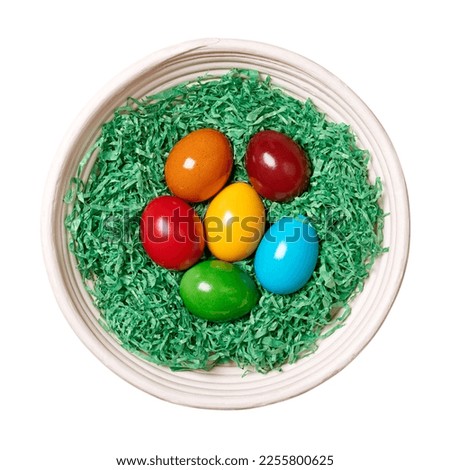 Wood wool nest with Easter eggs in a rattan basket. Colorful dyed Paschal eggs, arranged in a nest of green shredded paper. Group of hard boiled and rainbow colored chicken eggs, isolated, from above.