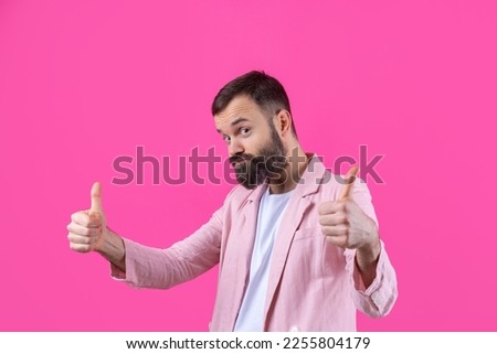 A man dressed in a pink jacket with a beard shows a thumbs up.