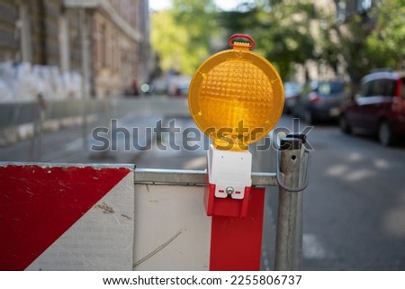 Yellow warning lamp attached to white and red barrier marking road works