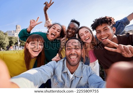 Happy multiethnic group of friends taking a selfie outdoors, having fun in sunny day. University students using phone app to take photos looking at camera.