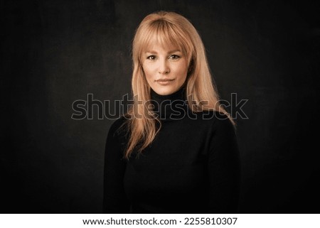 Beautiful smiling woman standing at isolated dark background. Blond haired woman wearing turtleneck sweater. Copy space. 