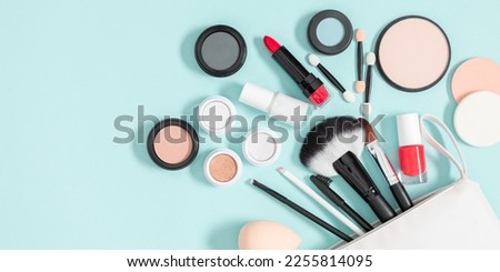 Set of different makeup cosmetics on blue background. White makeup bag and cosmetic beauty products. Flat lay, top view, copy space