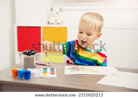 Cute boy drawing picture by using watercolors and couache indoors. Concept of leisure and kindergarten.