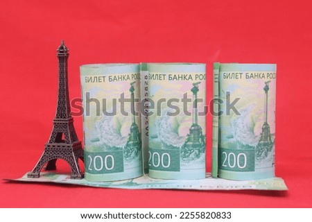 Souvenir Eiffel Tower stands on holiday money. Travel budget concept. Eiffel Tower and banknotes of 200 rubles on a red background