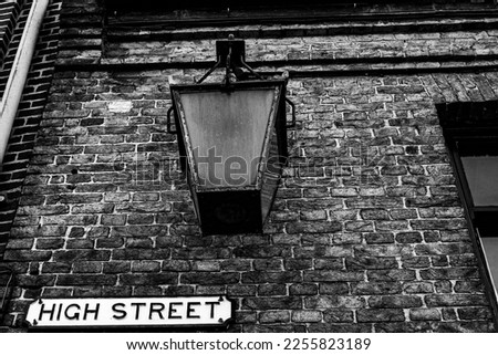 a vintage lamp hangs on a building above a street sign. Black and white.