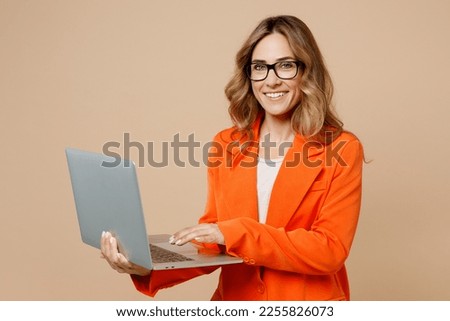 Young happy successful employee IT business woman corporate lawyer 30s wearing classic formal orange suit glasses work in office hold use laptop pc computer isolated on plain beige background studio