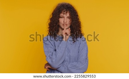 Shh be quiet please. Portrait of millennial woman 20 years old presses index finger to lips makes silence gesture sign do not tells secret. Young lovely curly haired girl on yellow studio background