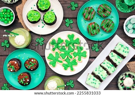 St Patricks Day theme desserts. Table scene over a dark wood background. Shamrock cookies, green cupcakes, brownies, donuts and sweets. Above view. Royalty-Free Stock Photo #2255831033