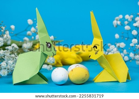 Two paper origami bunnies and an Easter eggs on a blue background. Crafts with your own hands for Easter