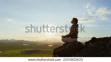 Man sitting on top of a mountain in a meditative pose taking breaths. Spiritual meditation retreat