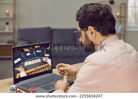 Young gambling man takes part in online poker tournament while relaxing at home. Man sits in front of laptop with poker chips. Concept of online gambling, chance, success, luck and gaming addiction. Royalty-Free Stock Photo #2255834247