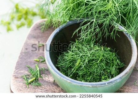 Just harvested cut fresh dills in bowl on brown cutting board on wooden table in summertime, cut dill leaves for flavouring food, flavouring herb concept Royalty-Free Stock Photo #2255840545
