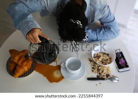 a beautiful girl in a denim shirt, her head rested on the table, she sleeps and pours coffee past the mug, the girl did not get enough sleep Royalty-Free Stock Photo #2255844397
