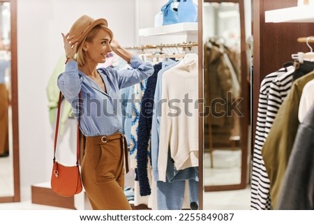 Side view portrait of smiling young woman trying on hats and accessories in luxury clothing boutique Royalty-Free Stock Photo #2255849087