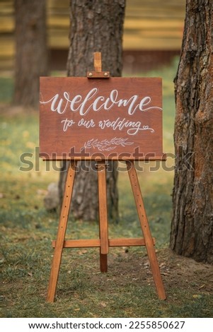 A wooden sign with the inscription "Welcome to our wedding" stands in a pine forest.
