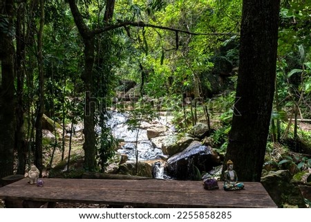 Rustic wooden table with bench and images of Buddha and stones, in front of the river in the woods, in the state of São Paulo, Brazil.