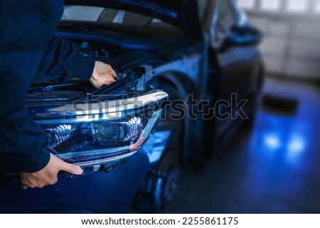 Mechanic with new car headlight in a workshop Royalty-Free Stock Photo #2255861175
